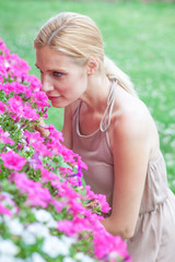 Fototapeta premium Beautiful blonde young woman smells flowers in a garden