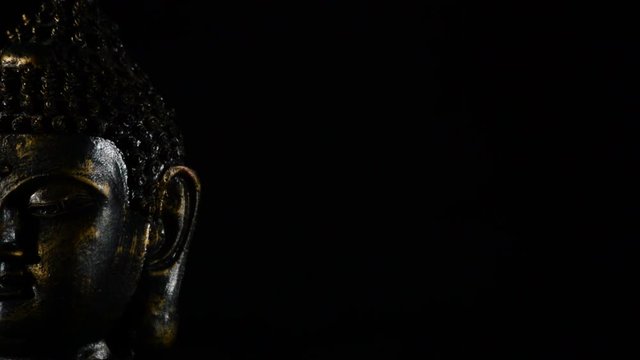Buddha face, deity buddhist, rotating at black background justify at left