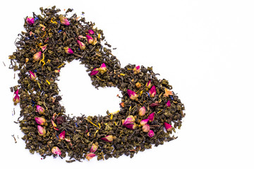 The leaves of green tea with rose buds and slices of dried fruits and wild flowers with the petals are laid out in the shape of a heart. Isolated on white background.