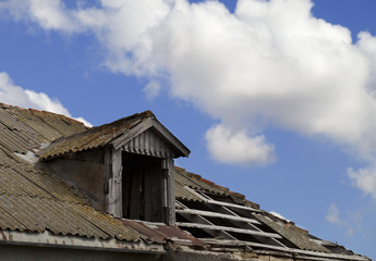 Old tile roof with holes and blue sky with clouds