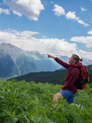 A woman is standing in a clearing, and indicates the mountain on a background of clouds