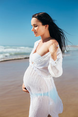 Fototapeta na wymiar Pregnant woman posing on a beautiful background of the sea. Pregnant young woman in black tunic in the seaside town.