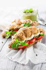 Crunchy wholegrain croissants with mozzarella, tomato and homemade pesto sauce on rustic white wooden background, selective focus