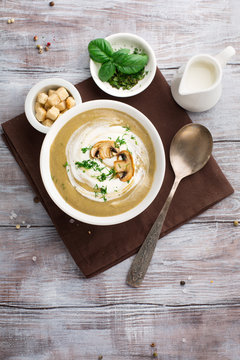 Champignon cream soup with fried mushrooms and fresh herbs on rustic white wooden table, top view