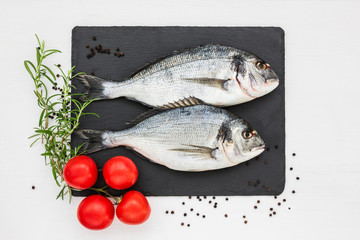 Fresh dorado fish on slate cutting board with rosemary and tomatoes. Top view, copy space