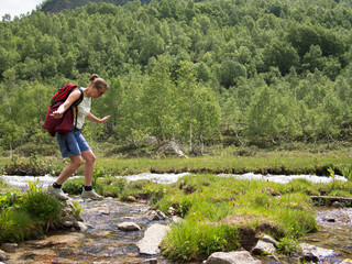 Tourist fearfully stands on the bank of a stream on a background of trees