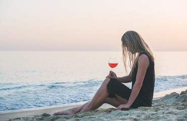 Fototapeta na wymiar Young blond woman relaxing with glass of rose wine on beach by the sea at sunset.