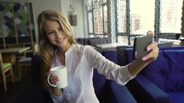 An attractive young blonde woman taking a self portrait on her cell phone at café