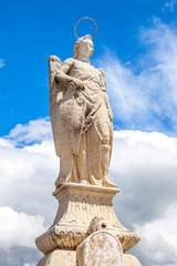 San Rafael Archangel statue in a sunny day and blue sky. The statue is the work of sculptor Bernabe Gomez del Rio and is at the center of the Roman Bridge in Cordoba, Andalusia, Spain.