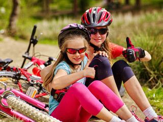 Bikes cycling family. Happy mother and daughter are sitting on country road near bicycles and shows thumb up.
