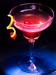 Fototapeta na wymiar Pomegranate alcohol cocktail with lemon and cherry decoration. Alcohol cocktail on black background.