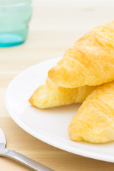 Croissant or Bread on White Dish on Wood Table with Spoon and Glass
