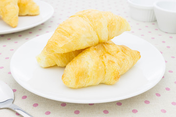 Croissant or Bakery on White Dish on placemat with spoon and tea cup
