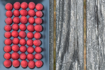 Fresh picked raspberries lined up on a black platter sitting on a deck
