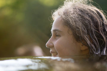 Child swimming in river with head above water. Young girl seen from viewpoint below water line, smiling with sunlight coming through hair