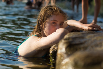 Child swimmer leaning against river bank. Young girl resting against stone on weir along River Avon, looking pensive with blue eyes
