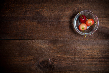 Obraz na płótnie Canvas berries cherries in a small bowl on wooden background dark color, three cherries in a small bowl on the boards
