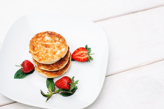 Pancakes with strawberry on white plate on wooden background, copyspace. Photo for restaurant menu