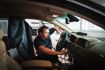 On-board computer tuning by serviceman at garage. Professional electrician working with electronic part of car. Modern technologies in automobile