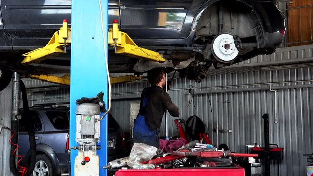 repairman repairing exhaust system on lifted up sedan car in car repair shop