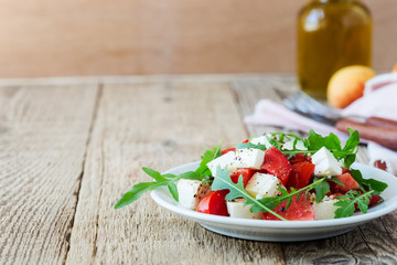Feta arugula salad with tomatoes on white plate, summer food