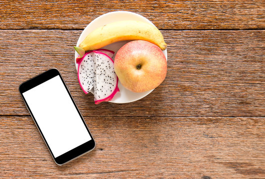 Smart phone with fruit (banana,appke,dragon fruit) on wooden flo