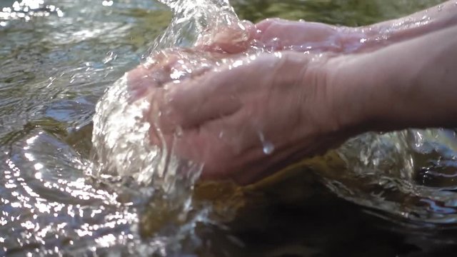 Man scooped up his hands clean water from the river and rises up, causing a lot of splashing. Slow motion, high speed camera, 250fps