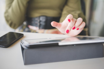 Close up on the hand of a young handsome caucasian girl using technological devices like tablet, tapping the screen - multitasking, technology concept