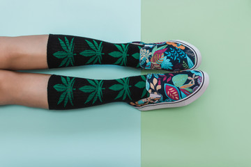 Woman's legs in socks and palm-printed slippers on light blue and green backgrounds. Flat lay, top view. Minimal concept.