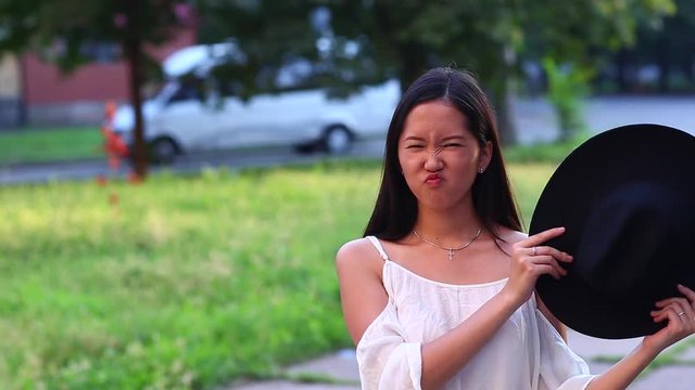 Eastern appearance with black straight hair. Cute female Young beautiful Asian girl in the green park background portrait, look to camera and showes tan, emotions hamming face happy