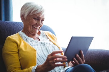 Smiling senior woman looking and laughing at her digital tablet - Powered by Adobe