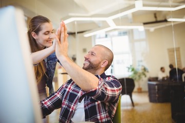 Businessman giving high-five to female colleague in office