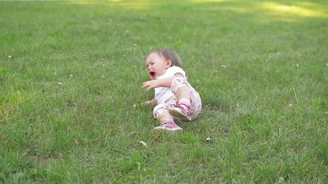 Children crying on green grass background, Small baby girl spending time outdoor on a warm summer day