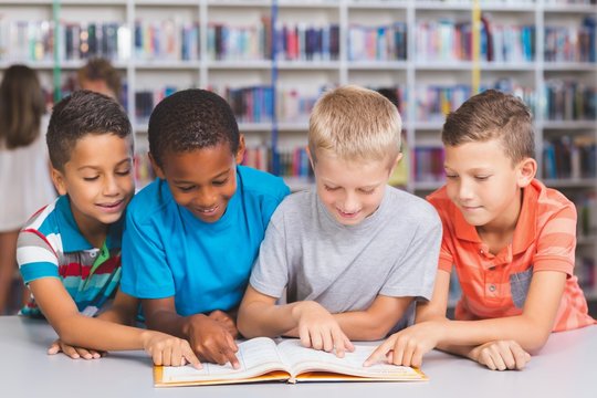 School kids reading book together in library