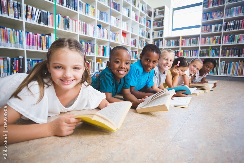 Poster smiling school kids lying on floor reading book in library
