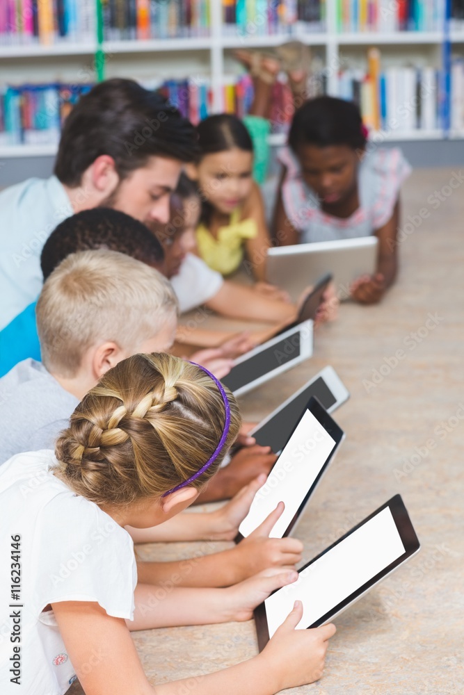 Poster teacher and kids lying on floor using digital tablet in library
