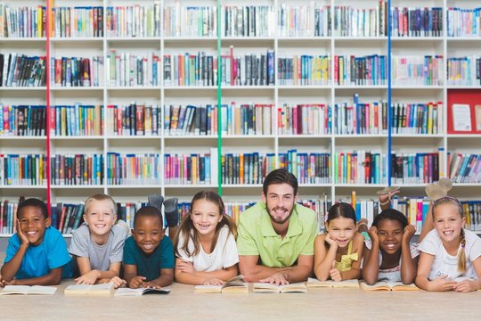 Teacher and kids lying on floor using digital tablet in library
