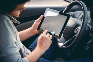 Young man driving a car with a tablet in hand, talking on mobile phone. Multitasking. Safe driving...