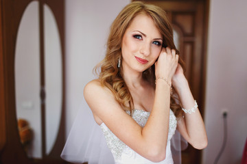 Fototapeta premium Bride smiles tender while putting on jewerly