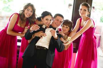 Groom leans to smiling bridesmaids