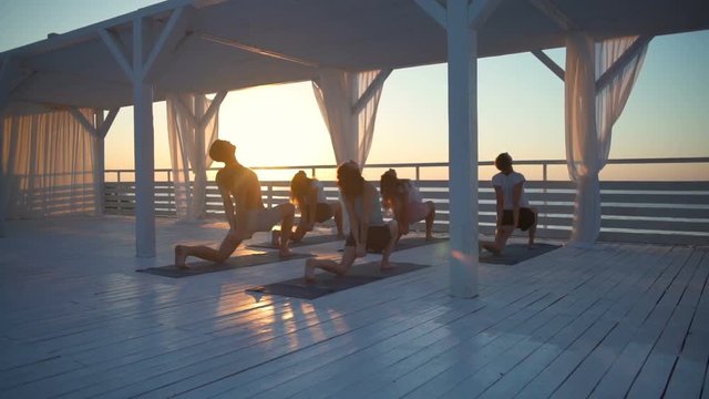 group of people on terrace by the sea practice yoga at dawn slow motion