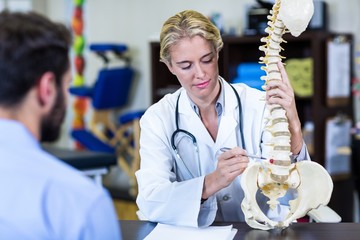 Physiotherapist explaining spine model to patient - obrazy, fototapety, plakaty