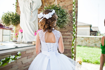 Fototapeta premium Portrait of cute little girl on white dress and wreath of first
