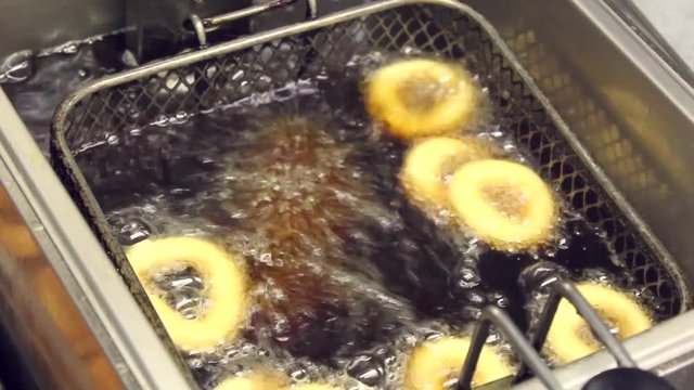 Cooking fried oil. Kitchen. Hand introduces doughnuts in fryer.