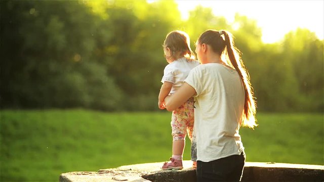 Happy mother with child enjoying together in sunny nature, Mom and daughter standing on the parapet