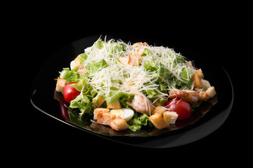 Caesar salad with prawns, cherry tomato and cheese on black plate
