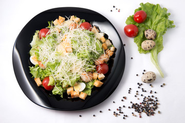 Caesar salad with prawns, cherry tomato and cheese on black plate on white background