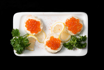 Sandwiches with red caviar on white plate on black background