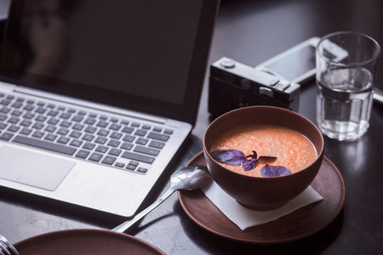 Picture of vegan dish soup represented on black wooden table near laptop computer in vegan restaurant or cafe.