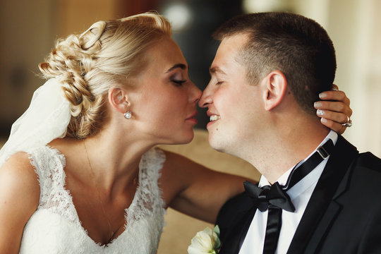 Blond bride touches groom's nose tenderly holding his head